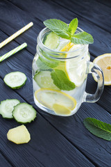 Wall Mural - Sassy  water  slimming or infused water with lemon, cucumber and ginger in the glass on the black wooden  background. Location vertical.