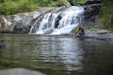 Man sitting at Khlong Nam Lai waterfall in Klong Lan national park, Kamphaeng Phet, Thailand