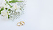 Flowers and two golden wedding rings on white background.