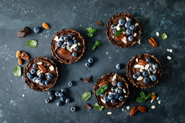 Healthy raw vegan dessert dates tartlets with chocolate cream of cashew, decorated with almond, pecan nuts and fresh blueberry