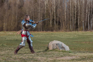 A knight on foot in armor and holding a sword in his hands shows combat attacks on the battlefield.