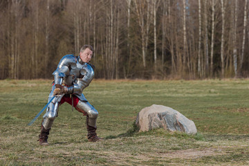 A knight on foot in armor and holding a sword in his hands shows combat attacks on the battlefield.