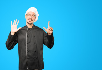 Happy young chef doing a number seven gesture with his hands