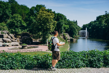 Sofia Park, Ukraine. Man with a backpack with a tourist map in a landscape park in summer. Guy in a T-shirt with a tourist map on the background of the lake with a fountain