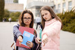 © Vitalii - Unhappy and regretful female students showing thumbs down in front of university building. Unhappy to study in university because of bad teaching stuff, lack of modern technologies and bullying