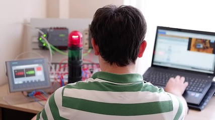 Back View of Young Man Who is Working Home Office and Making Online Education about PLC and Operator Panel Programming. Distance learning, also called distance education, e-learning or online learning