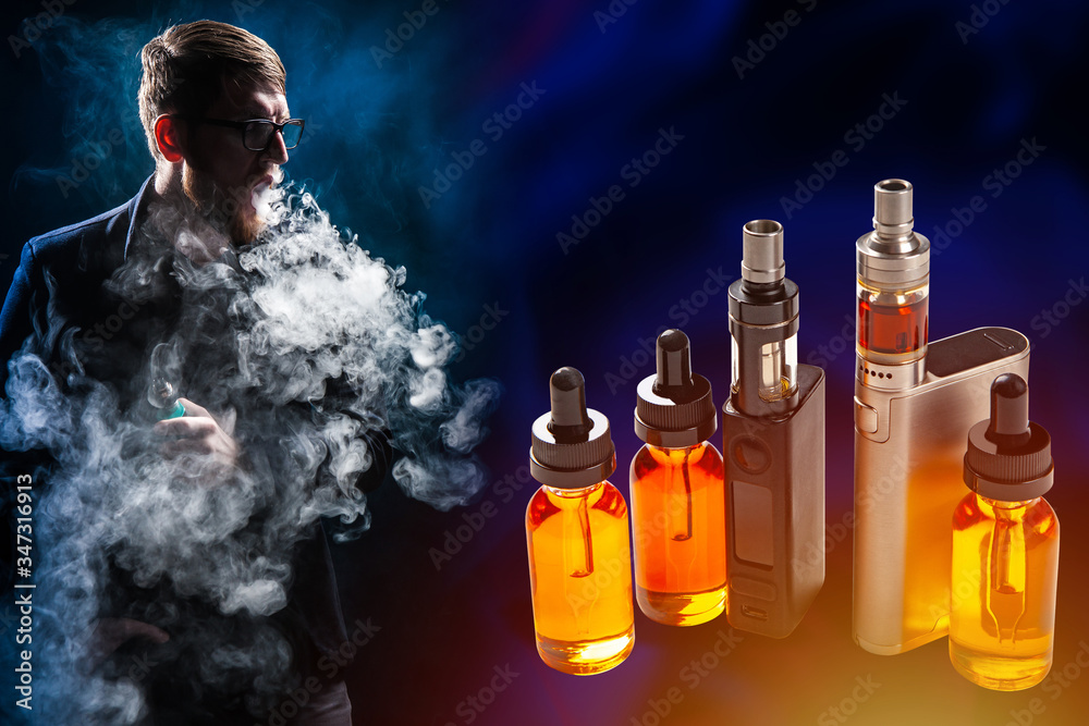 Vaping. Vaper crit and looks at vape devices. A man smokes steam in the dark. A Vaping. Vaper crit and looks at vape devices. A man smokes steam in the dark. A