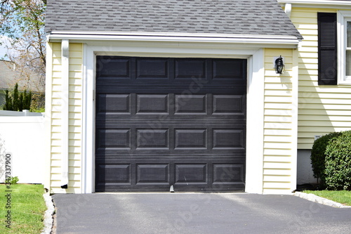 A  one car garage door painted in black  color in a typical single house.