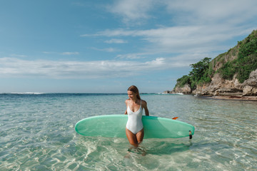 Rear view of beautiful sexy young woman surfer girl in bikini with blue surfboard on the beach. Young woman surfer girl waiting for a wave