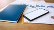 © Lek - Close up of smartphone and blue notebook on desk with paperwork of business and investment