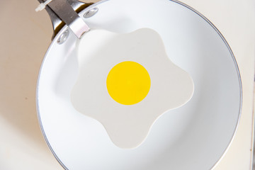 Particular objects in the kitchen. A white frying pan and an egg-shaped ladle over a wooden table.