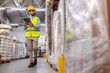 © Dusan Petkovic - Full length of supervisor in vest and protective helmet walking around warehouse and using tablet for checking out goods.