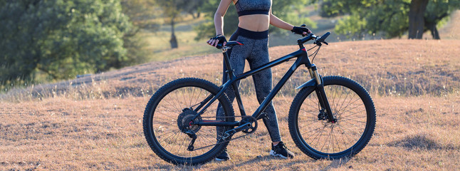 Girl on a mountain bike on offroad, beautiful portrait of a cyclist at sunset, Fitness girl rides a modern carbon fiber mountain bike in sportswear. Close-up portrait of a girl in a helmet and glasses