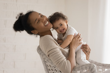 Wall Mural - overjoyed young african american mother sit in chair hug cuddle little newborn baby, happy biracial 