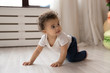 Cute little african American toddler infant go on hands and knees learn to walk on floor at home, small biracial baby girl child creep on fours, make first steps play indoor, childcare concept