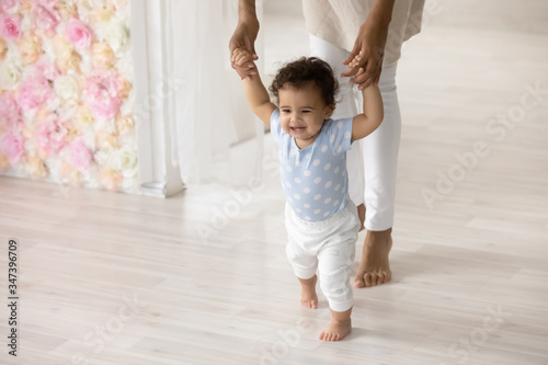 Cuadros en Lienzo Smiling little biracial toddler infant child make first steps at home holding mo
