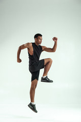 Do it Full length of young african man with muscular body in sports clothing jumping in studio against grey background