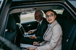 © Dusko - Good looking senior business man and his young woman colleague or coworker sitting on backseat in luxury car. They talking, smiling and using laptop and smart phones.