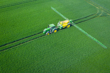 Wall Mural - Green Fields. Aerial view of the tractor spraying the chemicals on the large green field. Agricultural spring background.