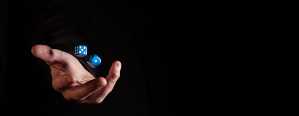 Male hand throwing blue dice cubes in the air against black background - narrow banner with copy space