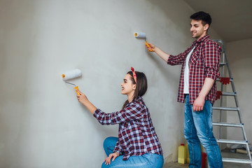 Repair, renovation and love couple concept - young family doing repair and painting walls together and laughing !