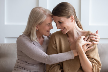 overjoyed senior mother and grownup daughter sit relax on couch hugging cuddling sharing secrets, sm