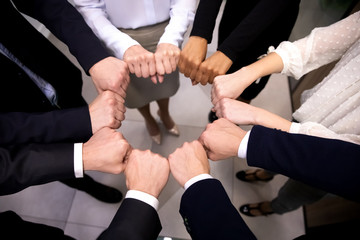 Close up top view diverse businesspeople in formal wear standing in circle puts fists together participating in team building activity, share common success provide support show loyalty, unity concept