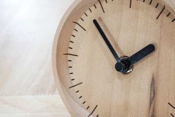 The close-up picture of the wooden table clock with a black dial showing about 2 o'clock on the wooden table as a background with warm light