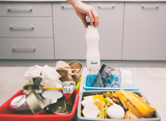 The woman throws plastic bottle can to the one of four container for sorting garbage