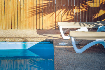 Wall Mural - deck chair rustic resort yard space of motel lounge furniture near swimming pool side under palm shadows on wooden palisade without people