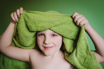 Cute funny blond boy with towel on green background. Child in towel with wet hair. Soft focus