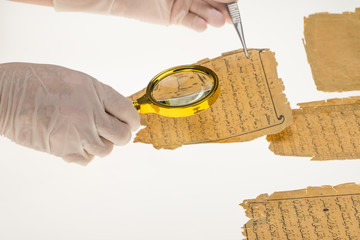 A researcher studies Arabic writing from the Koran using a magnifying glass and a table with a light. Paleography, the study of ancient Arabic writing