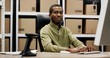 © VAKSMANV - African American postman sitting at desk in postal store working at computer