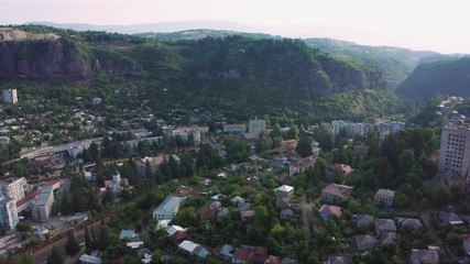 Wall Mural - Flight over of the center city, mining town Chiatura famous for its manganese mines being situated on Kvirila river. Evening summer twilight over the city and low clouds