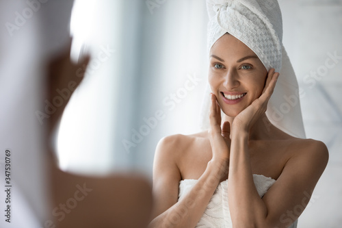 Fotomural After shower body and head wrapped in towel 35s woman looks in mirror touches mo