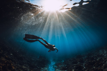 Wall Mural - Free diver woman with fins glides over coral bottom and amazing sun rays. Freediving underwater in sea