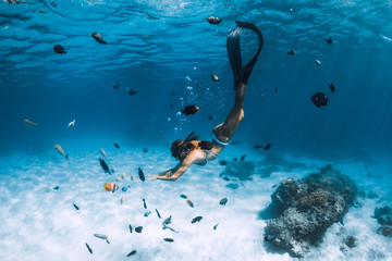 Wall Mural - Free diver girl with fins glides over sandy bottom with tropical fishes in blue sea