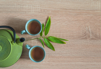 Tea time concept in asian style. Two chinese cups of tea, iron teapot and bamboo leaves on wooden background. Space for text, top view