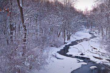 A partially frozen stream winds its way through a snow-covered winter landscape.