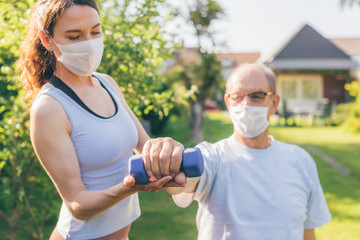 Senior man making physiotherapy session with young doctor (woman) - concept of physical therapy during or after covid-19 outbreak - focus on the hand with dumbbell