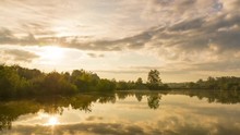 Side move Timelapse sunrise over lake sun rises behind a line of stoma on the shore and gradually changes orange color to daylight with reflection on water surface Hustopece Becvou Czech Republic