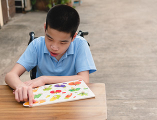 Asian Special need child on wheelchair interested in skills development toy on home nature background,Education for disabled children style,Boy plays fruit jigsaw puzzles,Happy disability kid concept.