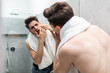 © F8  \ Suport Ukraine - Young man standing in front of mirror and touching his face in bathroom