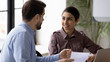 © fizkes - Close up indian smiling businesswoman listening businessman about successful finance report looking at leader. Diverse woman and male manager discuss and looking decision in negotiation.