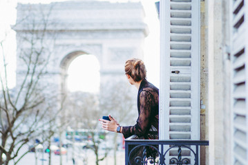 Attractive  yang woman in pajama is drinking coffee on balcony in the morning in city Paris. view of the triumphal arch.