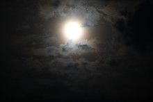 Beautiful Night Sky Background. An Indistinct Image Of A Full Moon In The Dark In A Fog Surrounded By Gray, Pale-lit Fluffy Clouds Of Gloomy Tones.The Mystical Picture