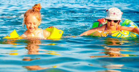 Portrait of  happy child girls playing and swimming in the sea. Kids having fun outdoors with water. Summer vacation and healthy lifestyle concept. Horizontal image.