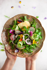 Wall Mural - Delicious summer salad with edible flowers, vegetables, fruit, microgreens and cheese. Woman holding plate with salad, top view. Clean and healthy eating concept.