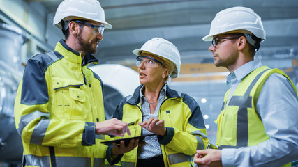 Wall Mural - Three Heavy Industry Engineers Stand in Pipe Manufacturing Factory, Use Digital Tablet Computer, Have Discussion. Large Pipe Assembled. Design and Construction of Oil, Gas and Fuels Transport Pipeline