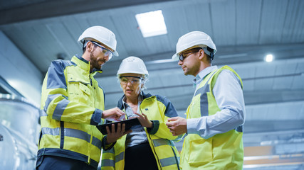 Wall Mural - Three Heavy Industry Engineers Stand in Pipe Manufacturing Factory, Use Digital Tablet Computer, Have Discussion. Design and Construction of Large Oil, Gas and Fuels Transport Pipeline. Low Angle